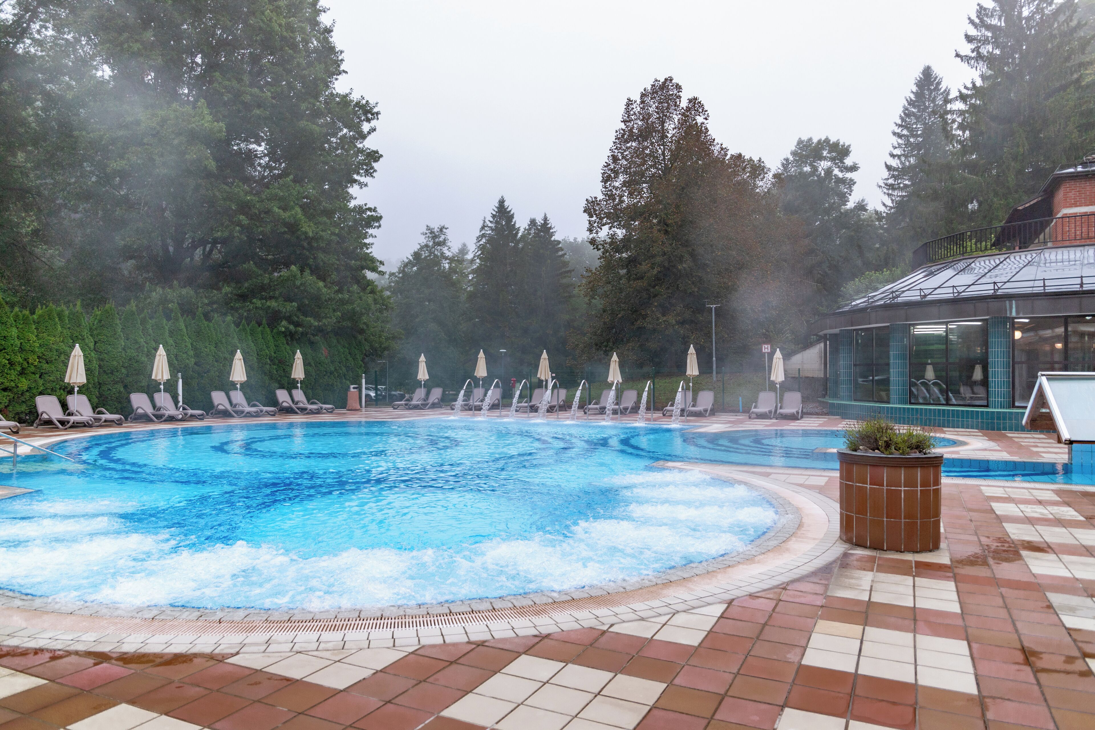 A swimming pool with lounge chairs and a hot tub area, surrounded by trees.