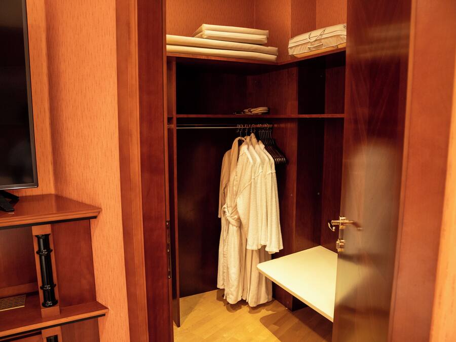 A wooden closet with hanging robes, a shelf with folded towels, and a bench.