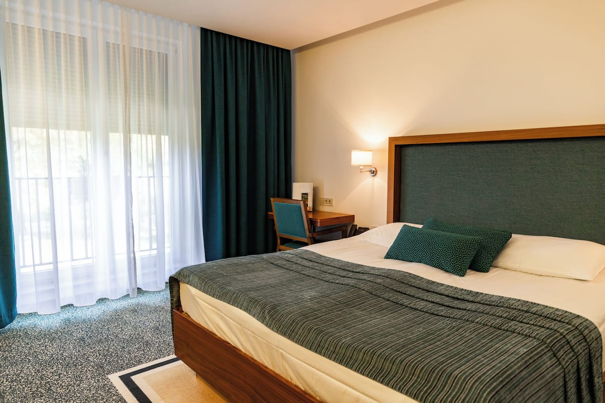 Une chambre d’hôtel avec un grand lit, un bureau, une chaise, une lampe et une fenêtre avec des rideaux.