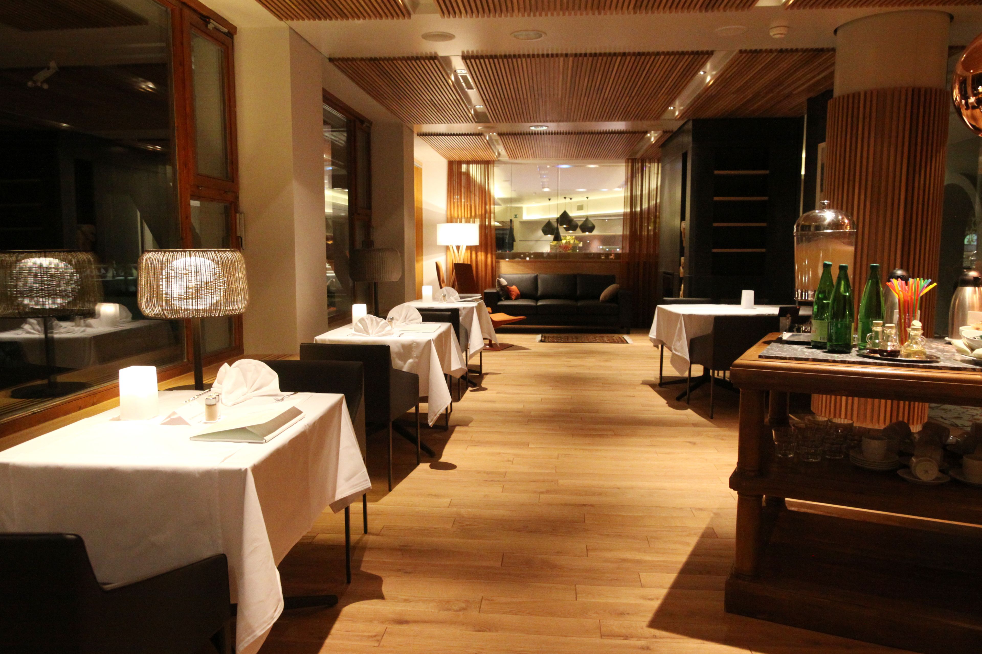 En hotellrestaurang med dukade bord, en soffa i bakgrunden och ett trägolv.