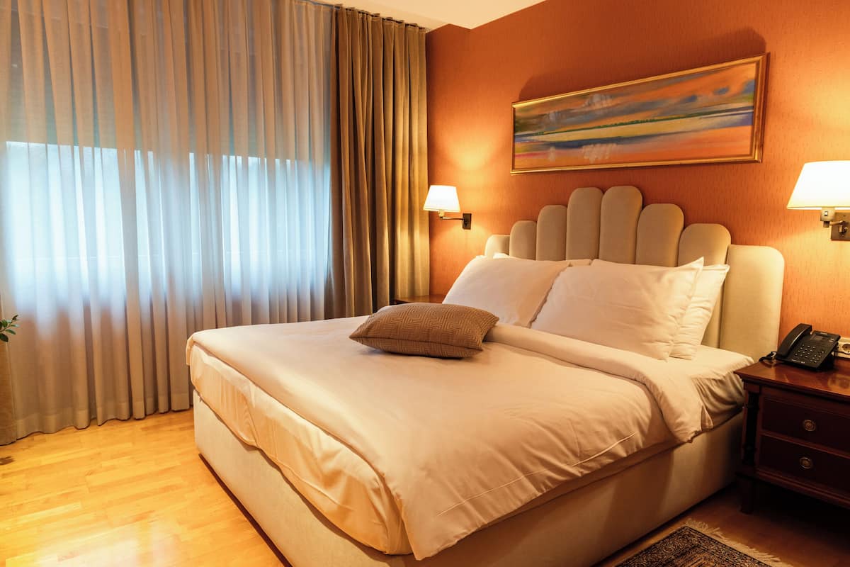 Une chambre d’hôtel avec un grand lit, deux lampes de chevet, un tableau au mur et une fenêtre avec des rideaux.
