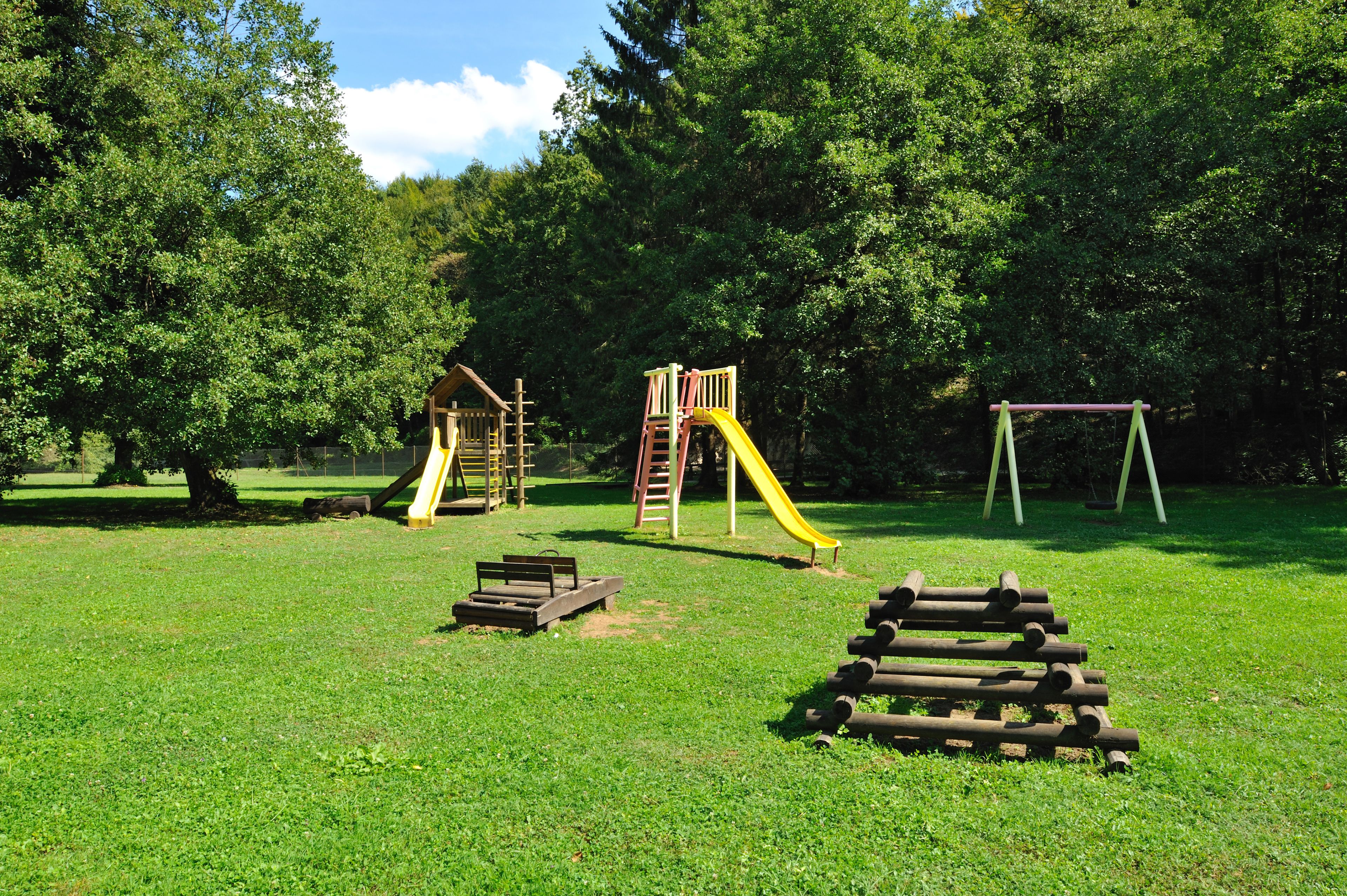 Une aire de jeux avec un toboggan, des balançoires et une petite structure en bois.