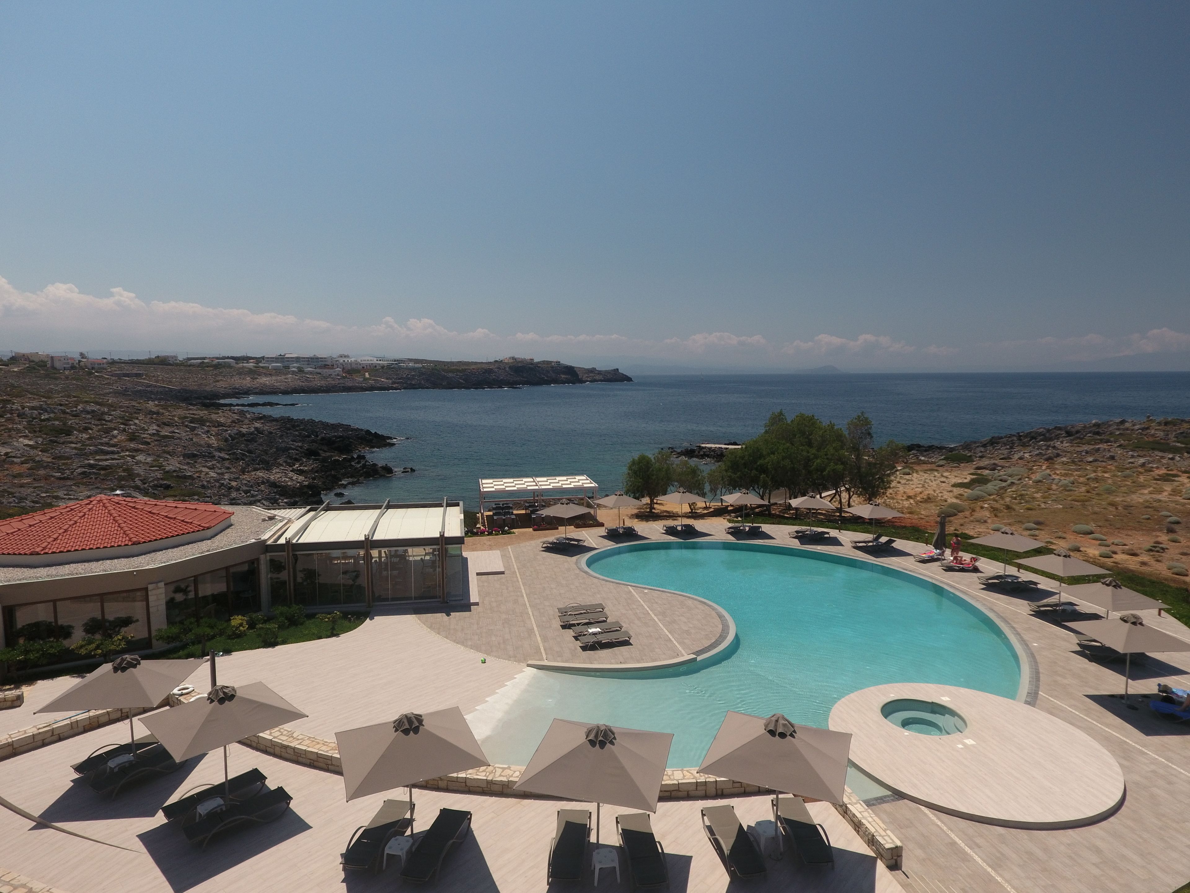 Una piscina de resort con tumbonas y sombrillas, vistas al mar y una costa rocosa.