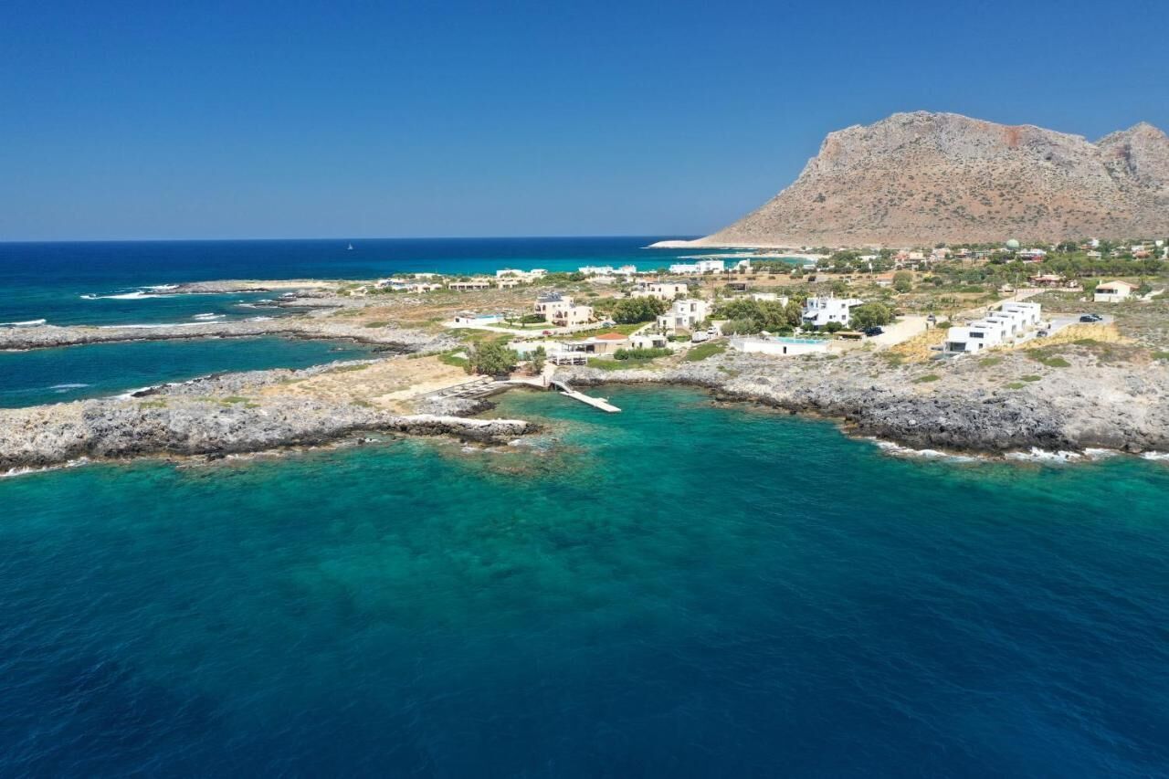 A coastal town with white buildings, clear turquoise waters, and a mountain in the background.