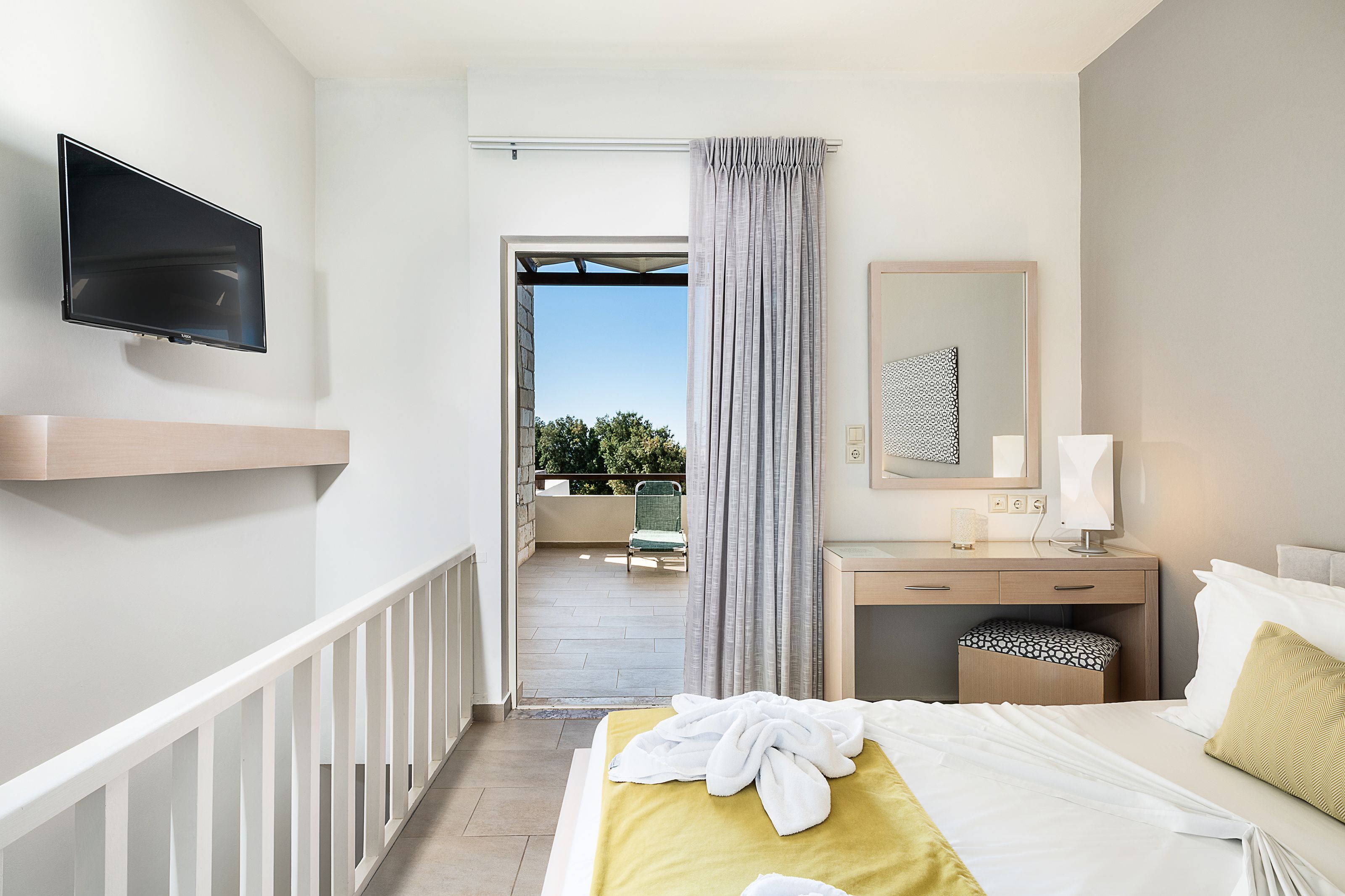 A hotel room with a bed, a desk, a TV, a balcony, and a view of greenery.