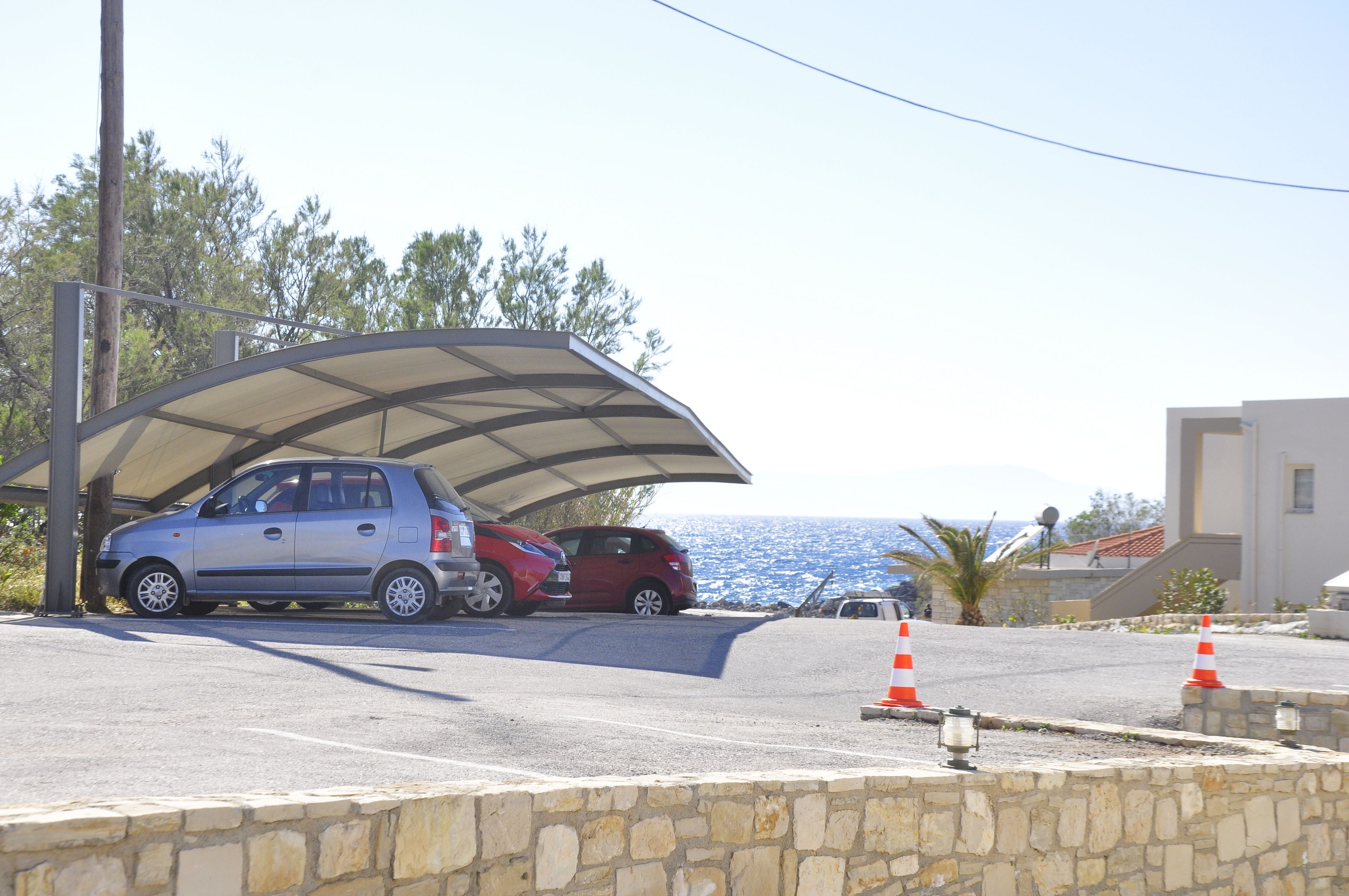 Un aparcamiento con marquesina cubierta, muro de piedra y vista al mar.