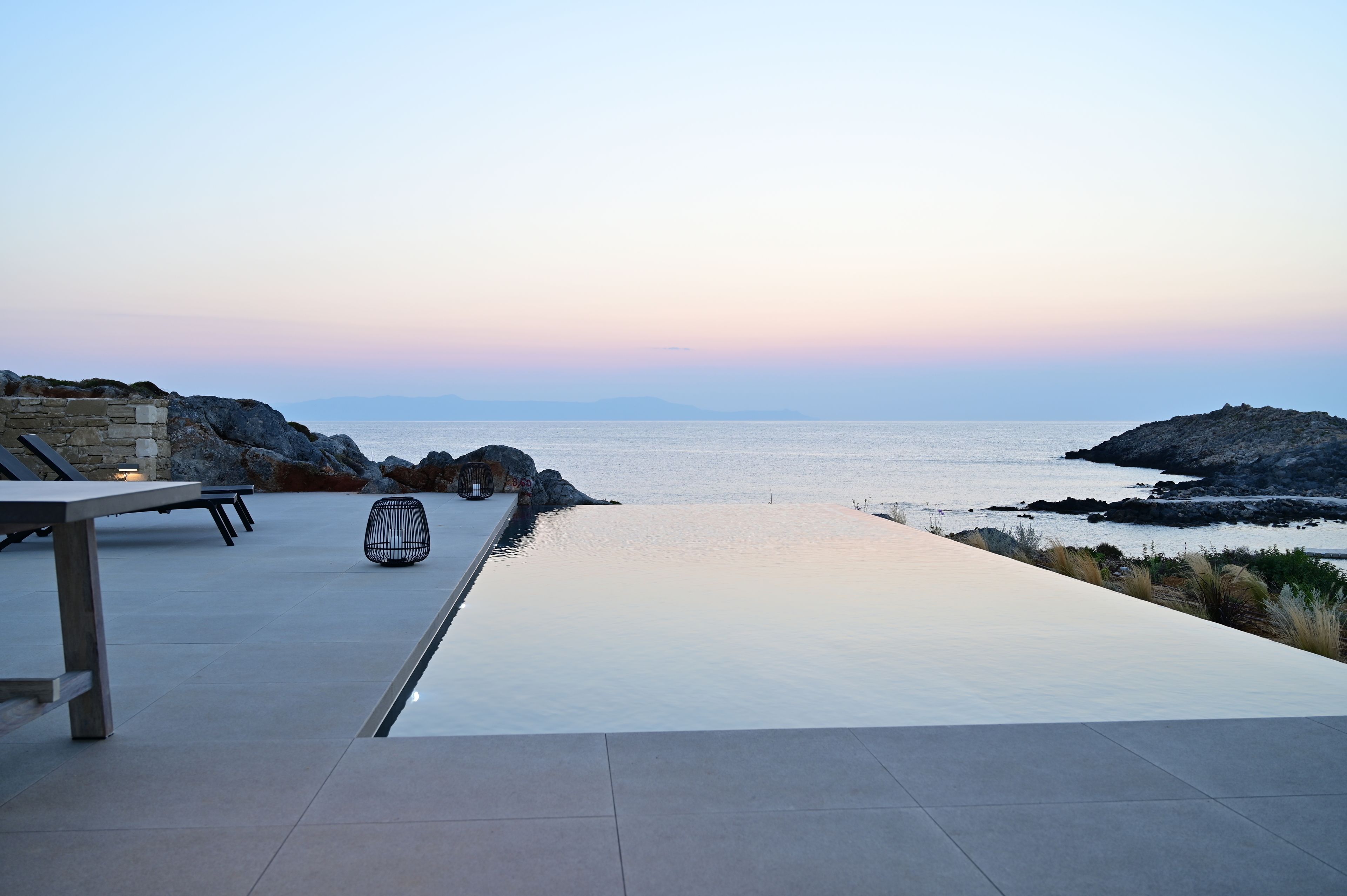 A serene outdoor terrace with a view of the sea, stone seating, and a modern table.