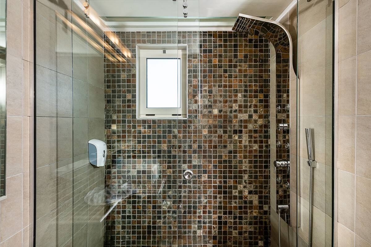 Ducha con puerta de vidrio, ventana y pared con azulejos.