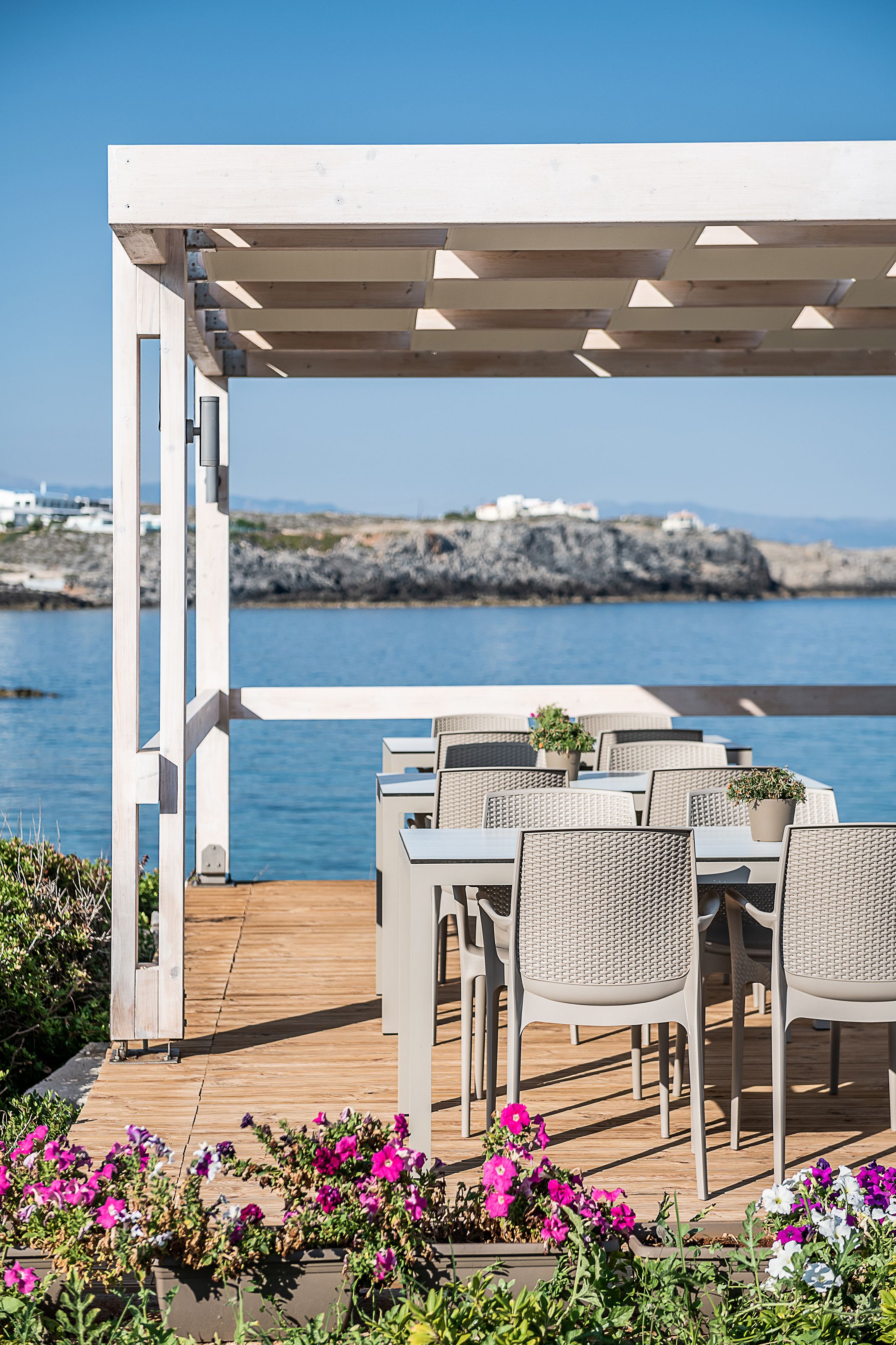Une terrasse en bois avec des sièges extérieurs, offrant une vue sur une étendue d’eau et un paysage rocheux.