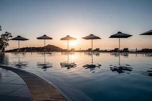 A pool with umbrellas and lounge chairs, surrounded by a calm water surface reflecting the sky. - Kavos Hotel (Chania)