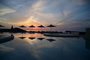 A serene pool area with umbrellas and lounge chairs reflecting the sunset. - Kavos Hotel (Chania)