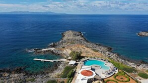 An aerial view of a coastal resort with a swimming pool, lounge areas, and rocky terrain. - Kavos Hotel (Chania)