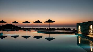 Un área de piscina tranquila con sombrillas y sillones de descanso, reflejando el cielo y el agua.
