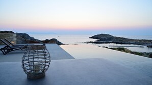 A serene poolside view overlooking a calm sea at sunset, with a wicker lantern and lounge chairs. - Kavos Hotel (Chania)