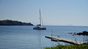 A sailboat on calm waters near a dock with a rocky coastline in the background.