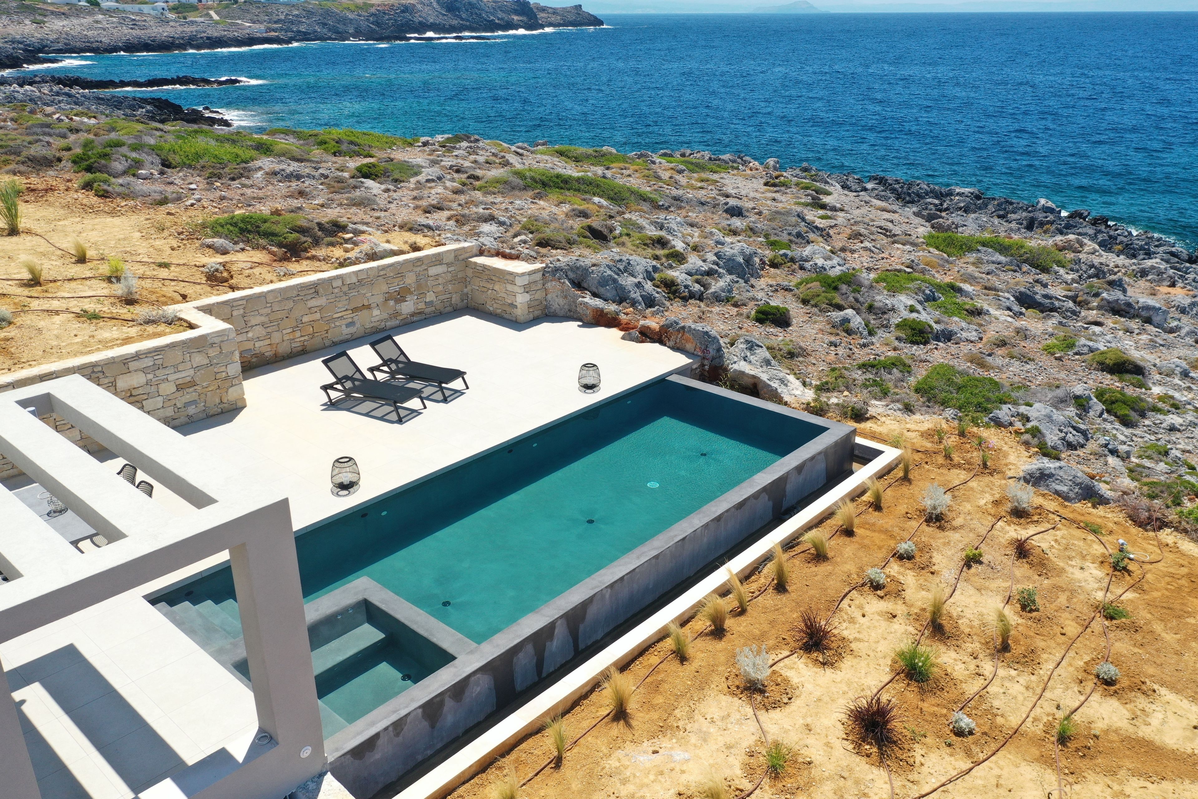 Un espace piscine extérieur moderne, doté d’une terrasse en pierre, de chaises longues et offrant une vue sur l’océan.