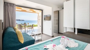 A modern hotel room with a large bed, a sofa, a TV, and a view of the sea. - Kavos Hotel (Chania)