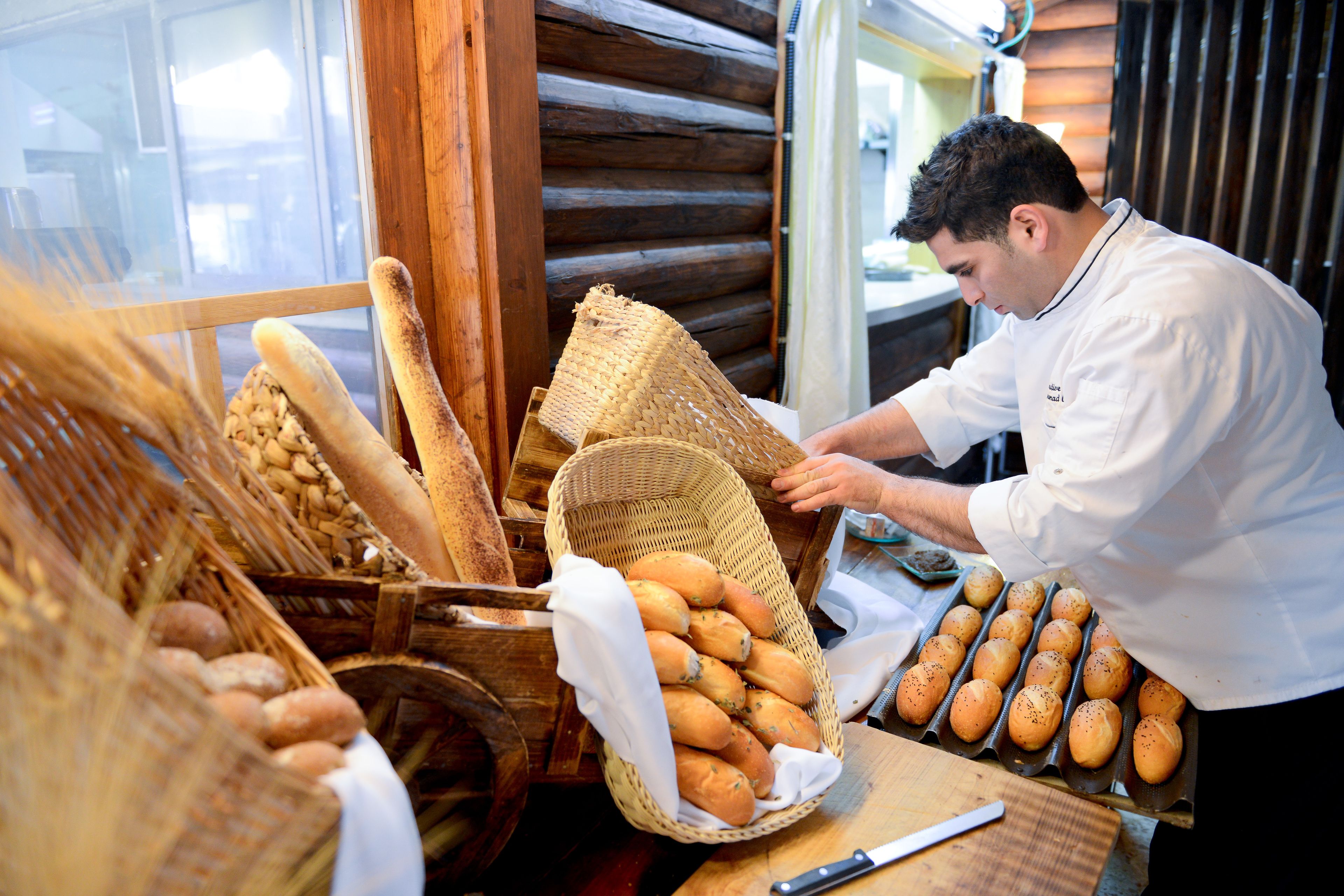 A bakery with wooden walls and a window. Baskets of bread and a knife on a cutting board are visible.