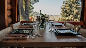 A dining table set with plates, glasses, and a bottle, with a view of trees and a building through a window. - Logos hotel in Yad Hashmona (Mateh Yehuda)