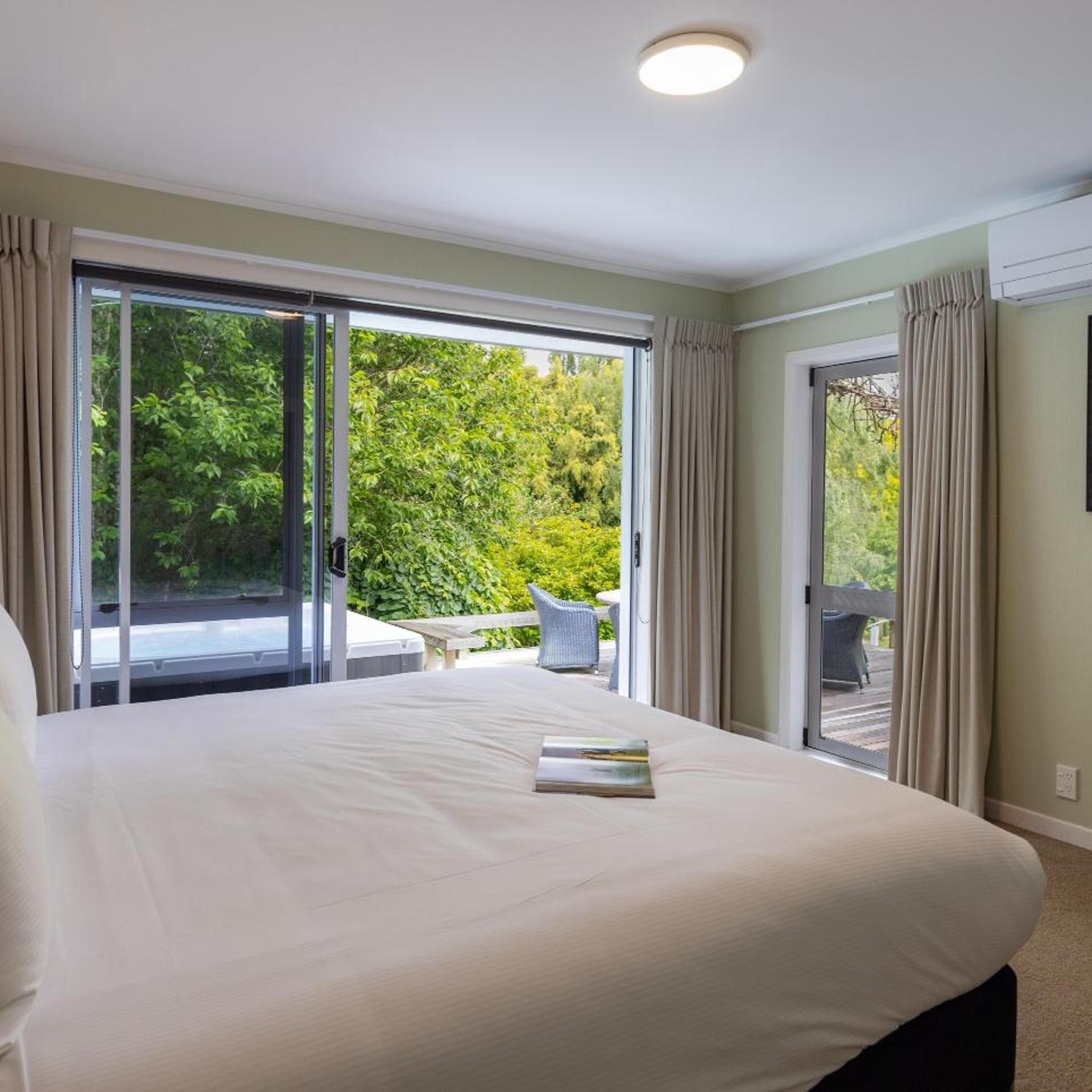 A bedroom with a large bed, a sliding glass door leading to an outdoor area, and a ceiling light.