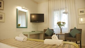 Een hotelkamer met een bed, een televisie, twee fauteuils, een kleine tafel met een bloevas en een spiegel.