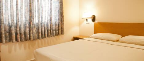 A hotel room with a bed, a nightstand, a lamp, and a window with curtains.
