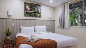 A hotel room with a bed, pillows, a blanket, a painting of birds, a plant, and a window with curtains. - Chambers Wildlife Rainforest Lodges (Lake Eacham)
