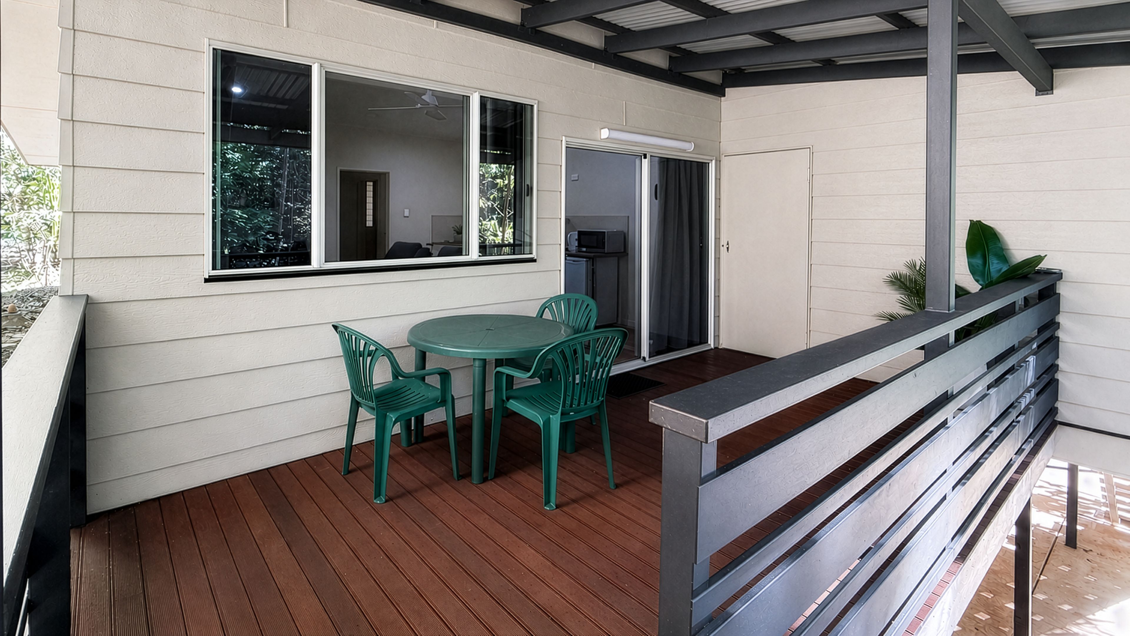 A covered outdoor area with a wooden deck, a table with chairs, and a metal railing.