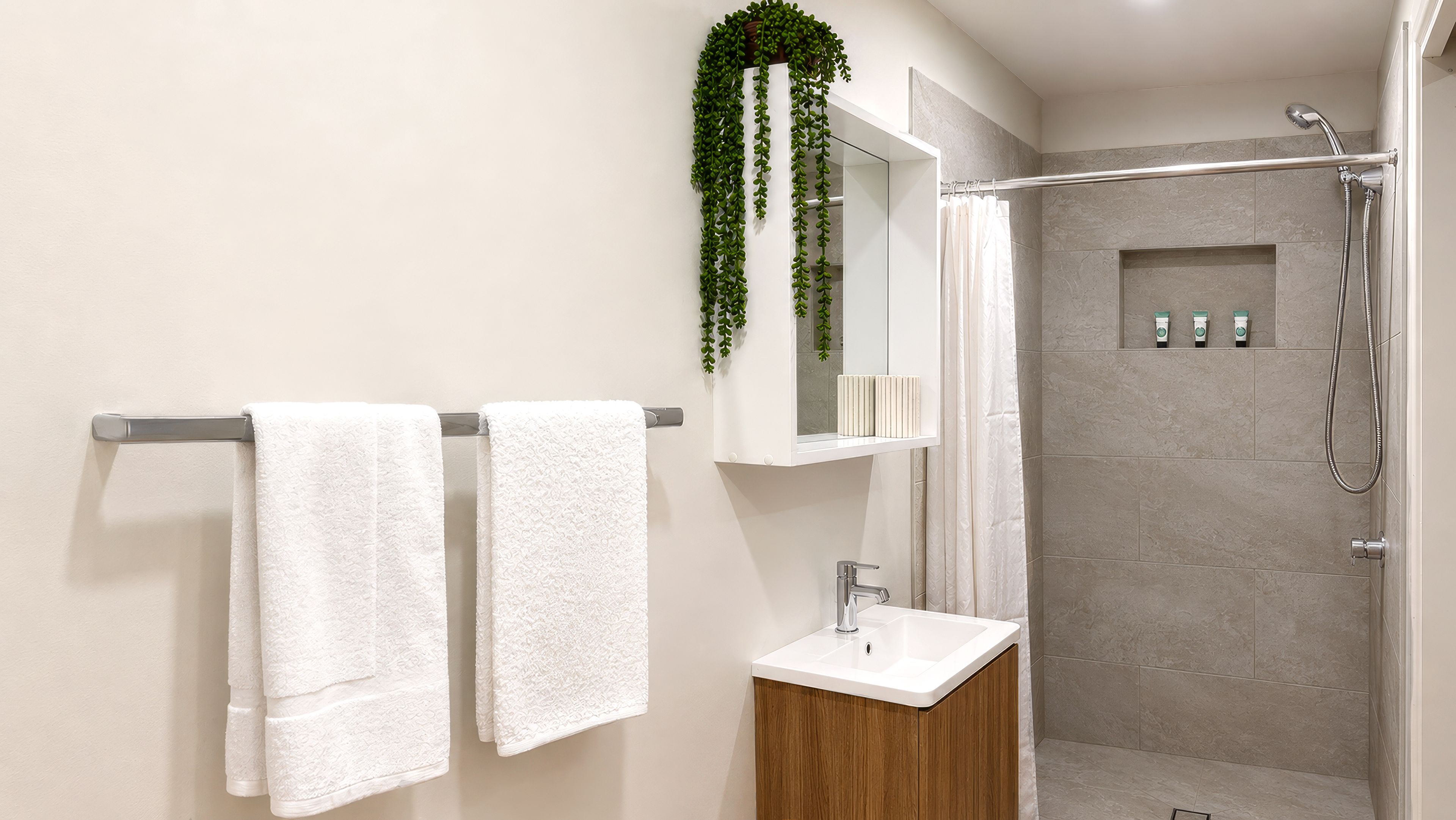 Un baño moderno con ducha, lavamanos y dos toallas colgadas en un perchero.