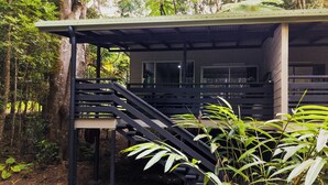 A covered outdoor area with a staircase leading to a building, surrounded by dense greenery.