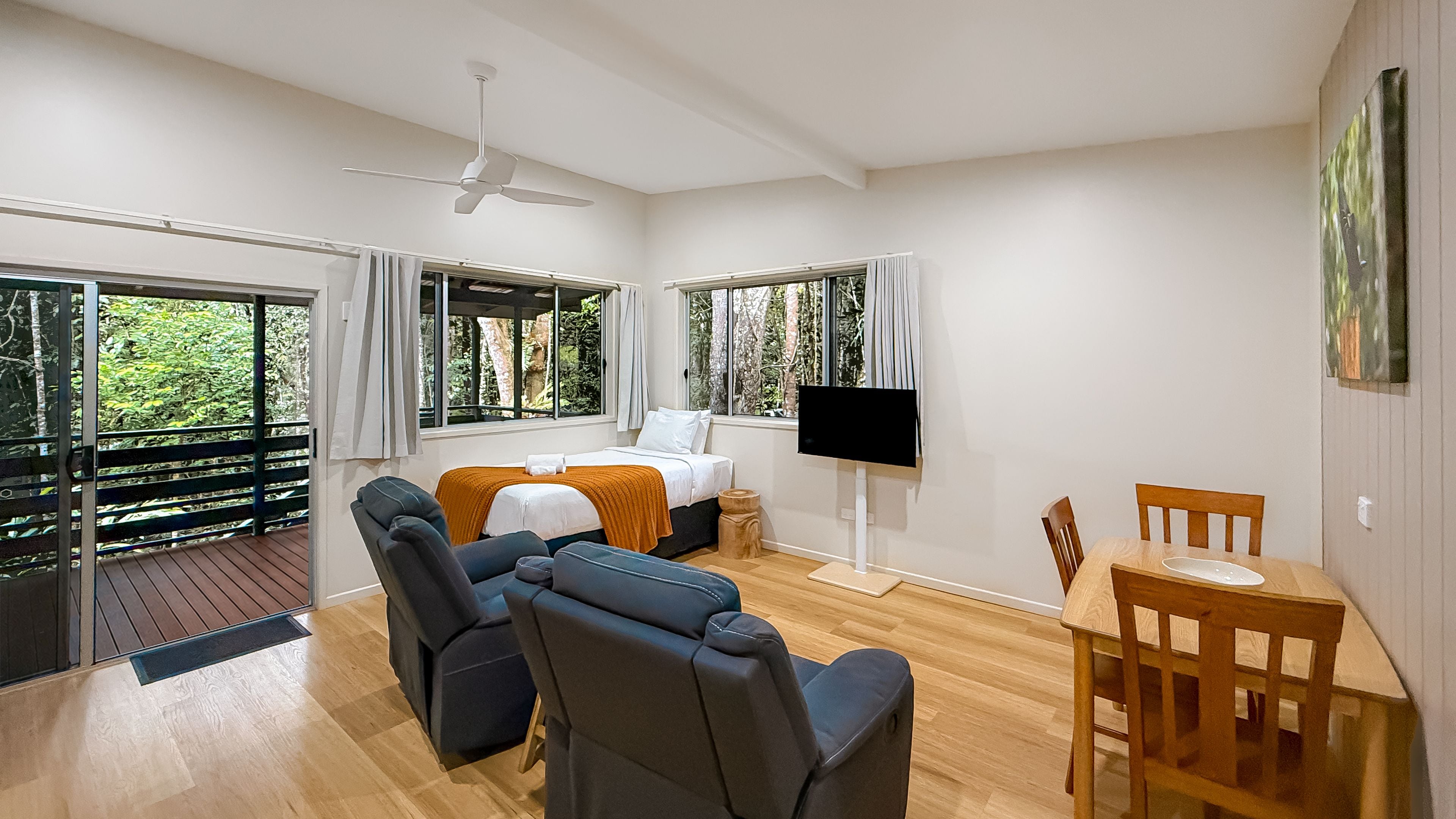 A room with a bed, seating area, dining table, TV, and large windows.