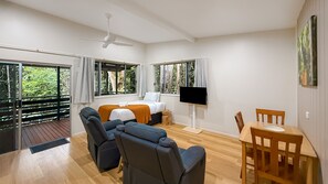 A room with a bed, seating area, dining table, TV, and large windows. - Chambers Wildlife Rainforest Lodges (Lake Eacham)