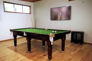 A pool table with balls, a cue stick, and a television on the wall.