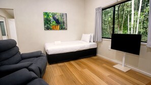 Quarto com cama, poltrona, televisão e janela com vista para árvores.