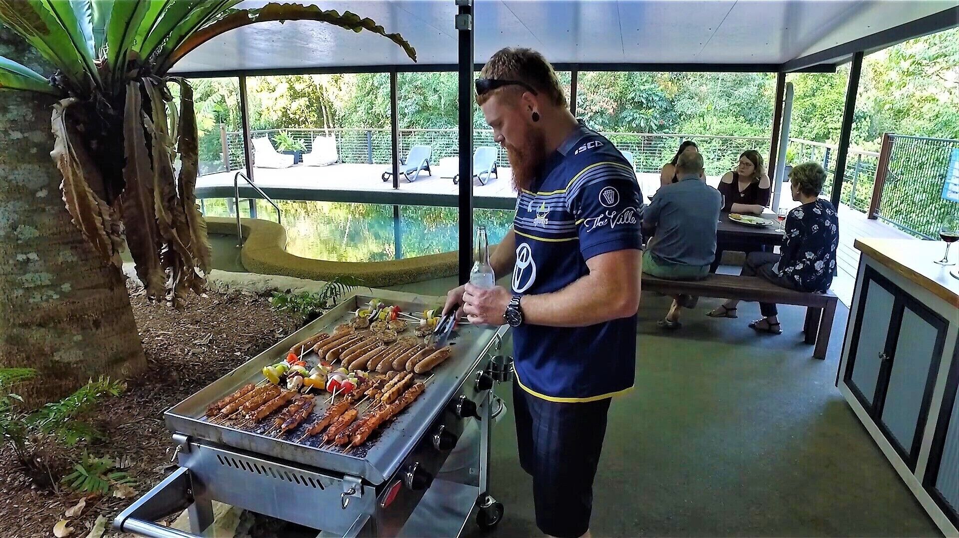 Eine Person grillt Würstchen und Spieße auf einem Grill.