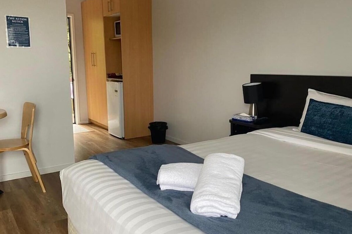 Una habitación de hotel con cama, escritorio, silla, armario y una pequeña kitchenette.