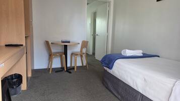 A hotel room with a bed, a small table with two chairs, a trash bin, and a door leading to another room.