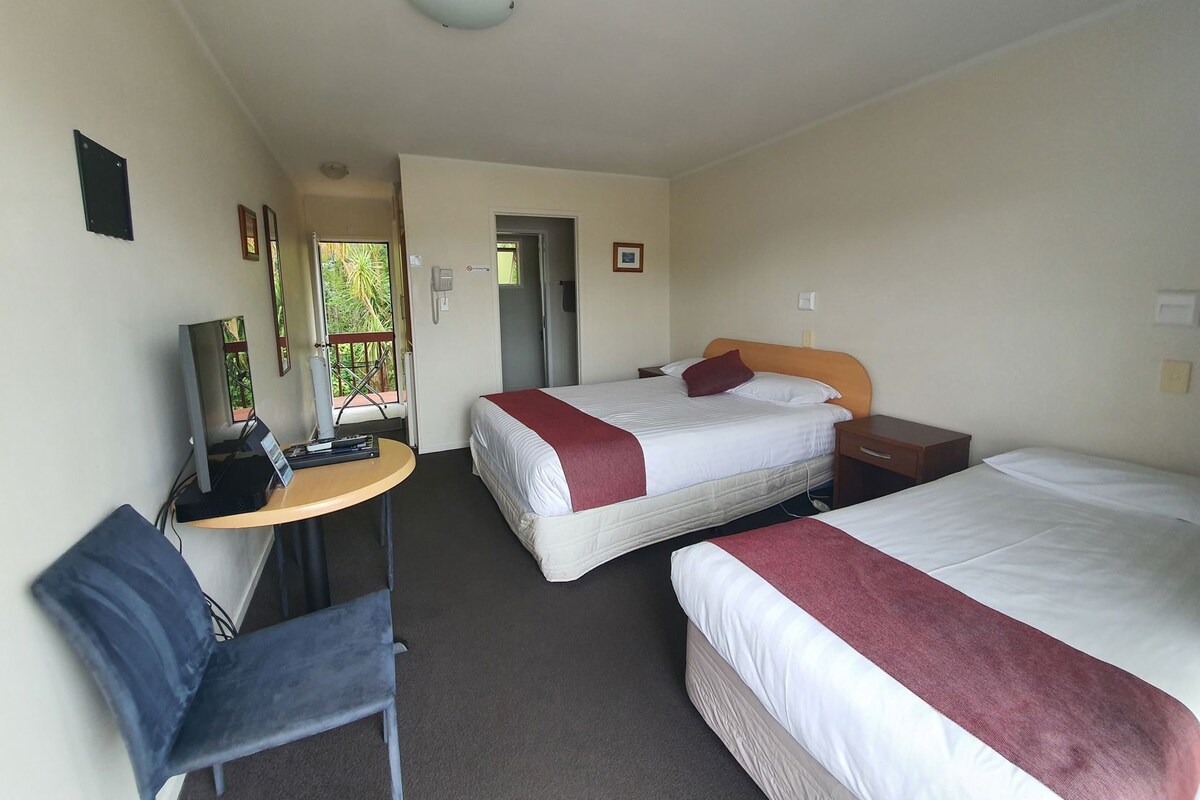 Habitación de hotel con cama, escritorio, silla, televisión y puerta que da a otra habitación.