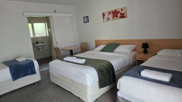 Habitación de hotel con tres camas, una mesita, una silla, un lavamanos y un cuadro en la pared.