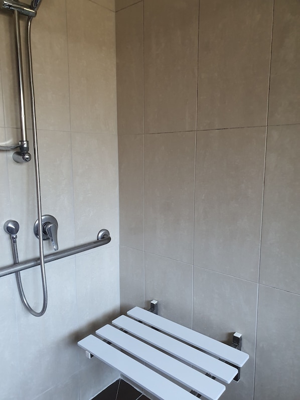 Zona de ducha con cabezal de ducha de mano y barra de apoyo.