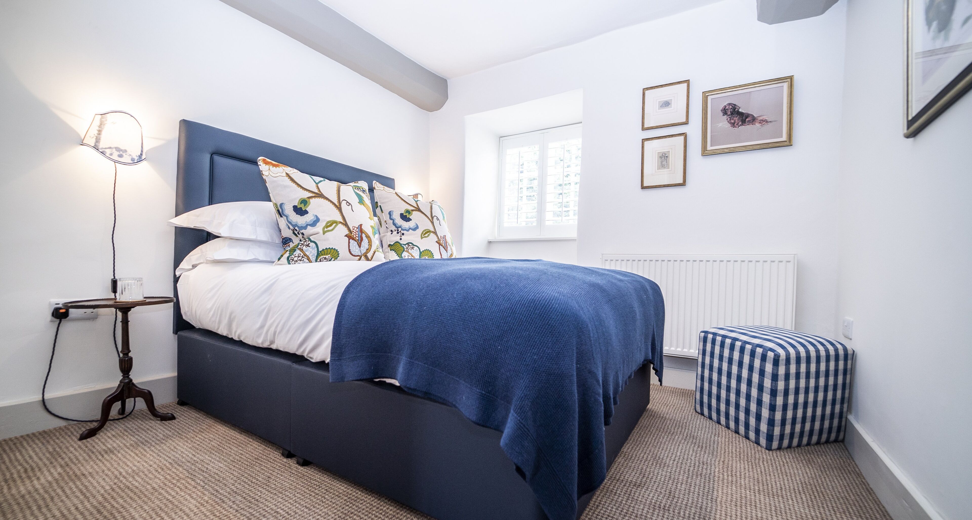 A bedroom with a bed, a bedside table with a lamp, a radiator, and a window.