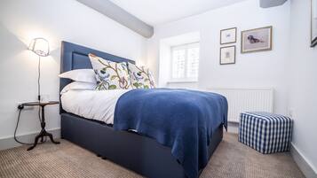 A bedroom with a bed, a bedside table with a lamp, a radiator, and a window.