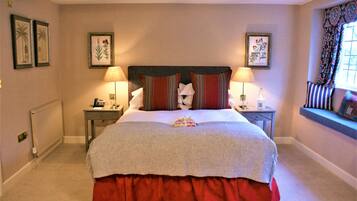 A neatly made bed with a red skirt, two bedside tables with lamps, and framed botanical prints on the walls.