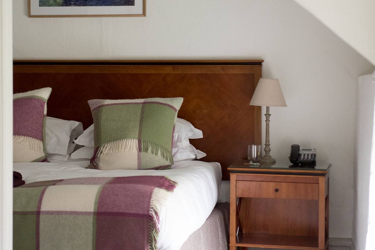 A bedroom with a bed, a nightstand, a lamp, a telephone, and a painting on the wall.
