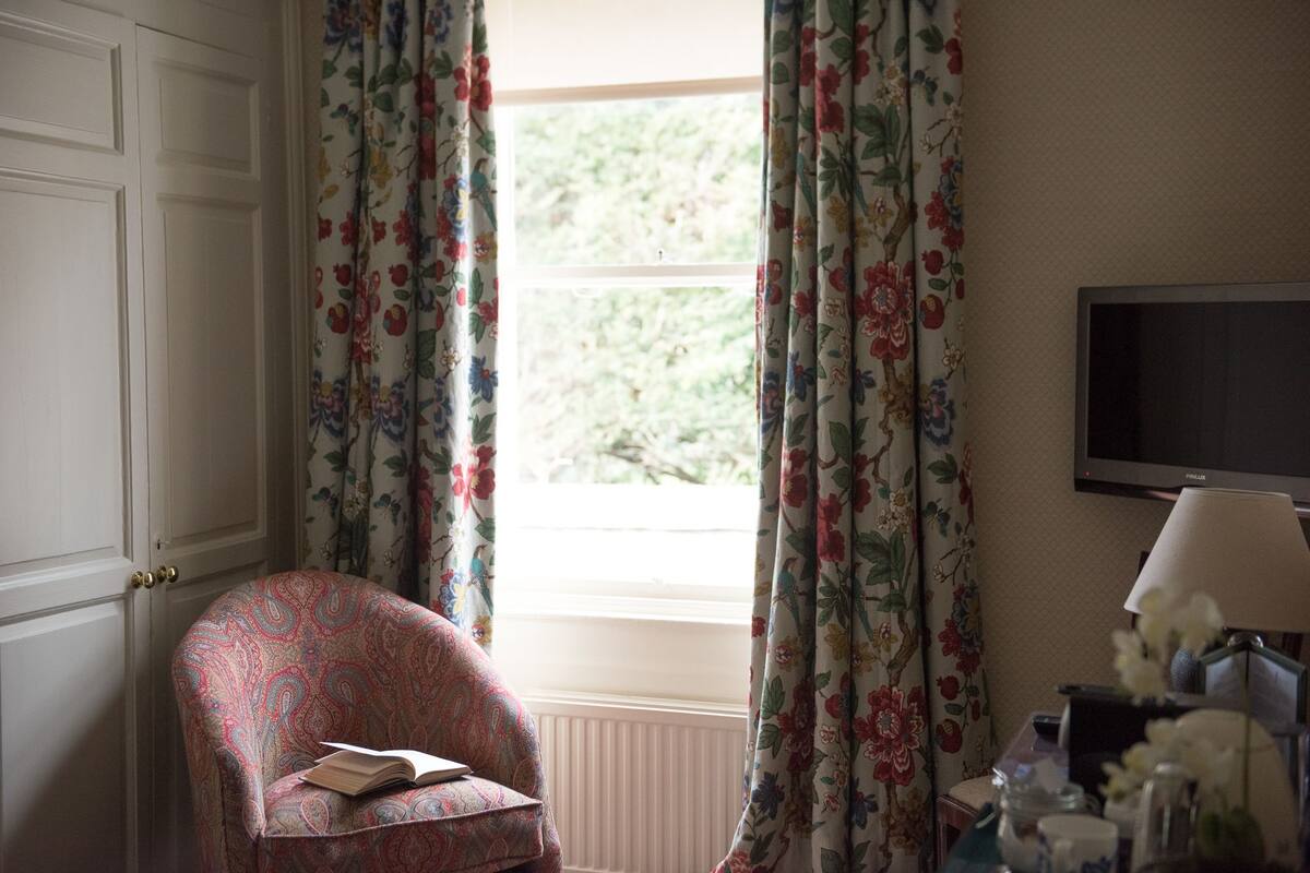 A room with a floral-patterned chair, a television, and a window with curtains.