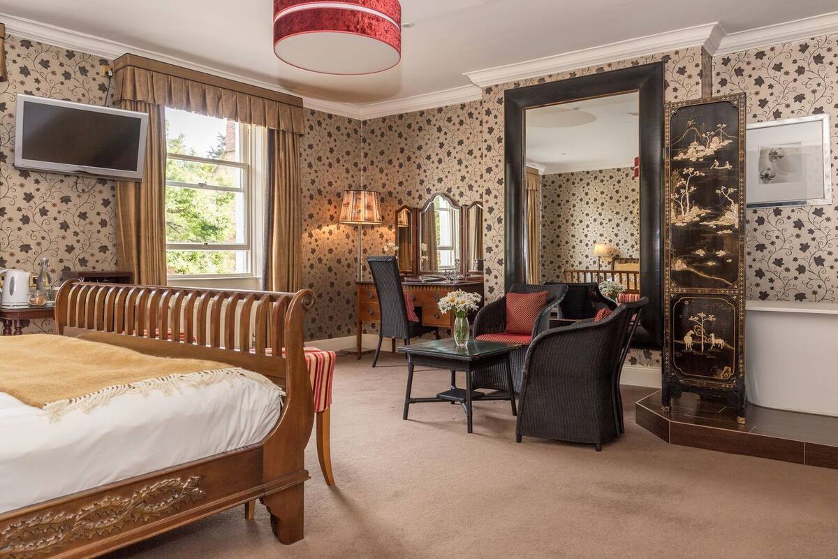 A hotel room with a large bed, a desk, a chair, a television, and a mirror.