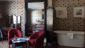 A room with a large mirror, a bathtub, and a dining area with red chairs and a table. - The Eastbury Hotel (Sherborne)