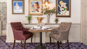A dining area with two upholstered chairs, a table with wine glasses, and three framed artworks on the wall. - The Eastbury Hotel (Sherborne)