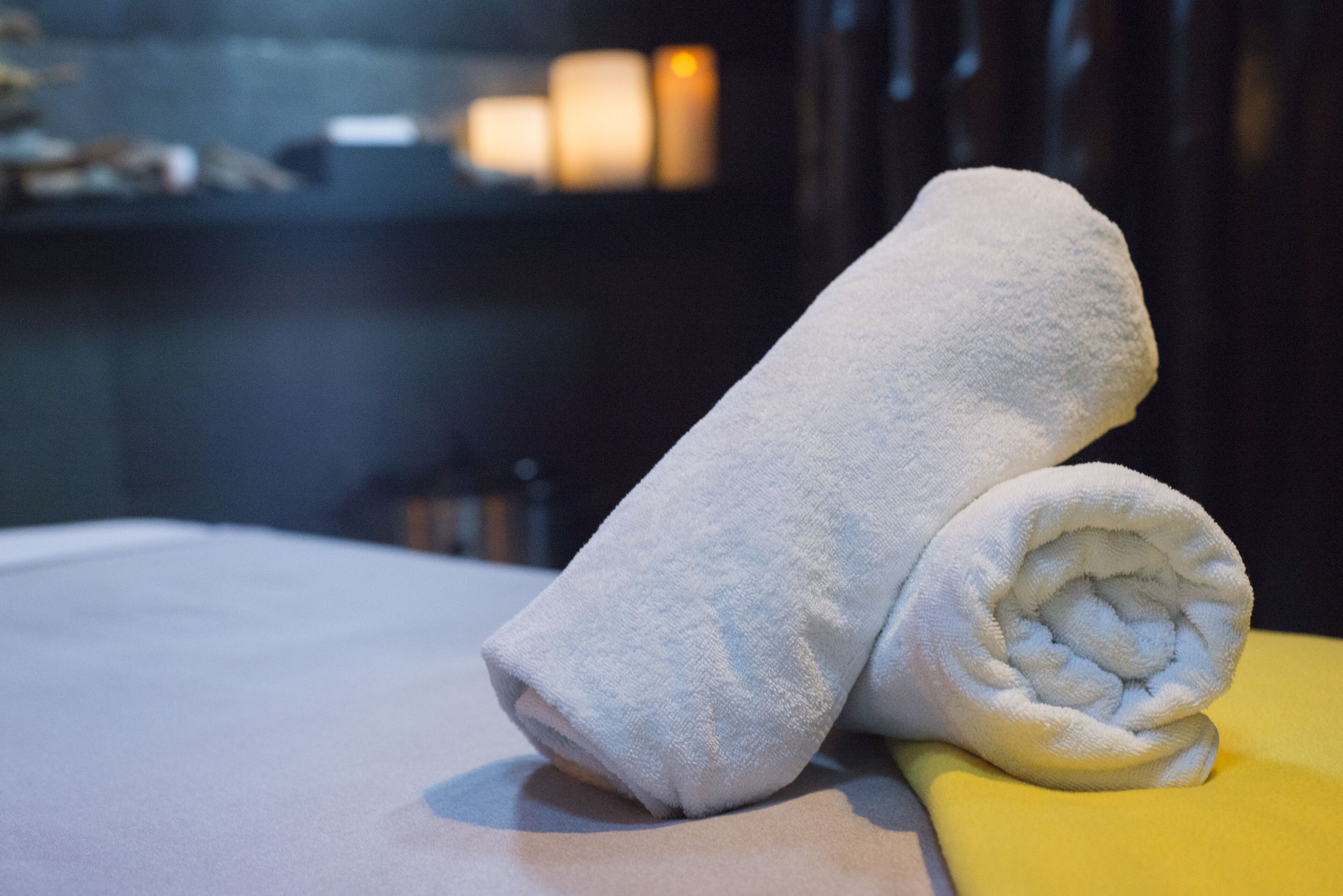 A neatly folded white towel on a bed with a yellow pillow.