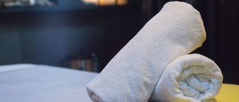 A neatly folded white towel on a bed with a yellow pillow.